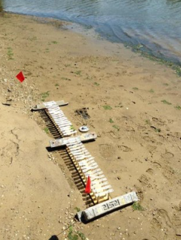 Numerous plastic swatches attached to sampling apparatus, secured in the environment with large dive weights. The sampling apparatus is set on a sandy beach with the river cutting through the top part of the image. Numerous plastic swatches attached to sampling apparatus, secured in the environment with large dive weights. The sampling apparatus is set on a sandy beach with the river cutting through the top part of the image.